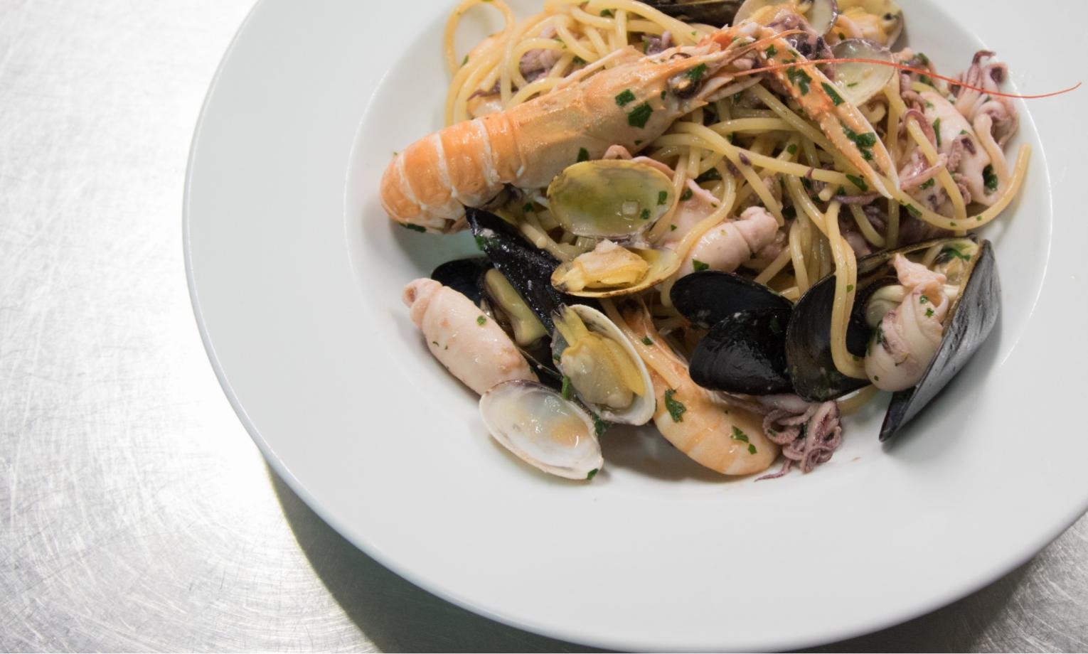 Spaghetti ai frutti di mare con scampi, cozze e vongole su piatto bianco.