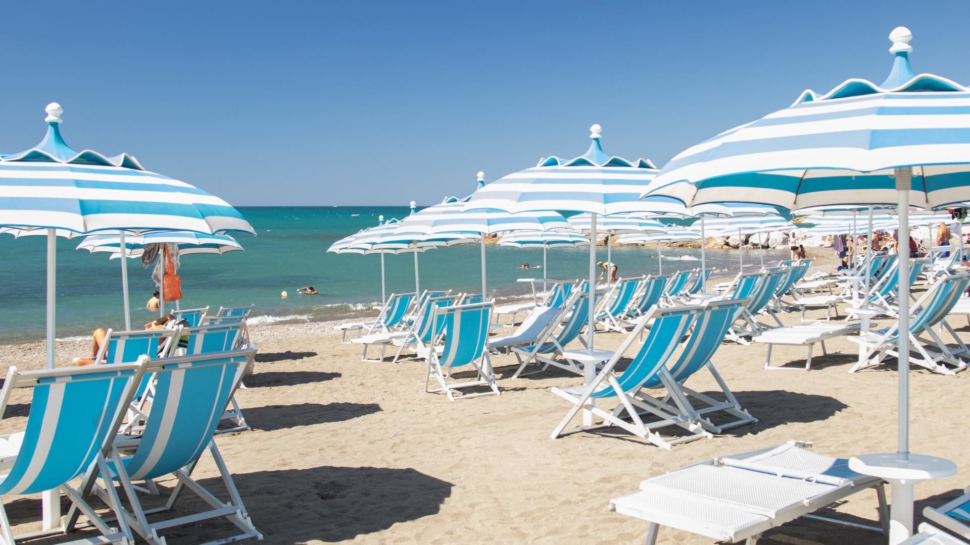 Spiaggia con ombrelloni e lettini blu e bianchi, mare calmo e cielo sereno.