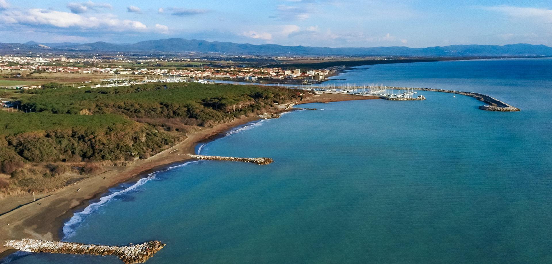 Vista aerea della costa con spiaggia, pineta e porto turistico.