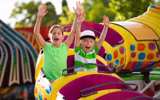 Bambini felici su una giostra colorata nel parco divertimenti, mani alzate.