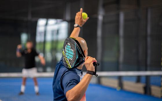 Giocatore di padel pronto a servire su un campo blu al chiuso.