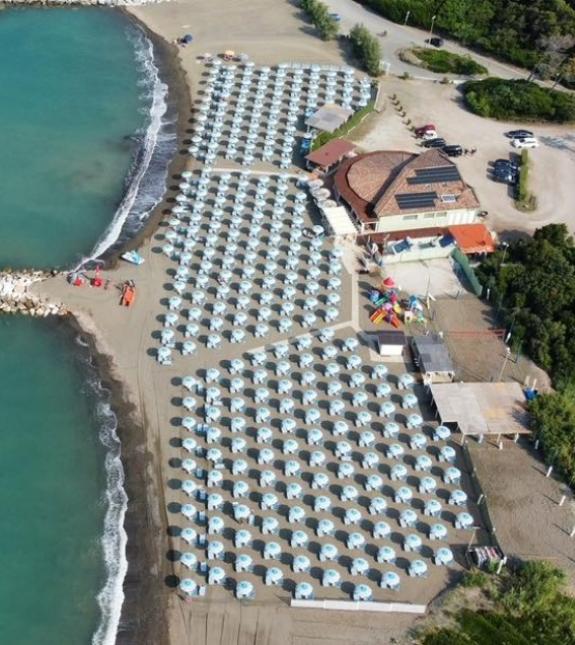 Spiaggia con ombrelloni azzurri, vista dall'alto, vicino a un edificio e al mare.