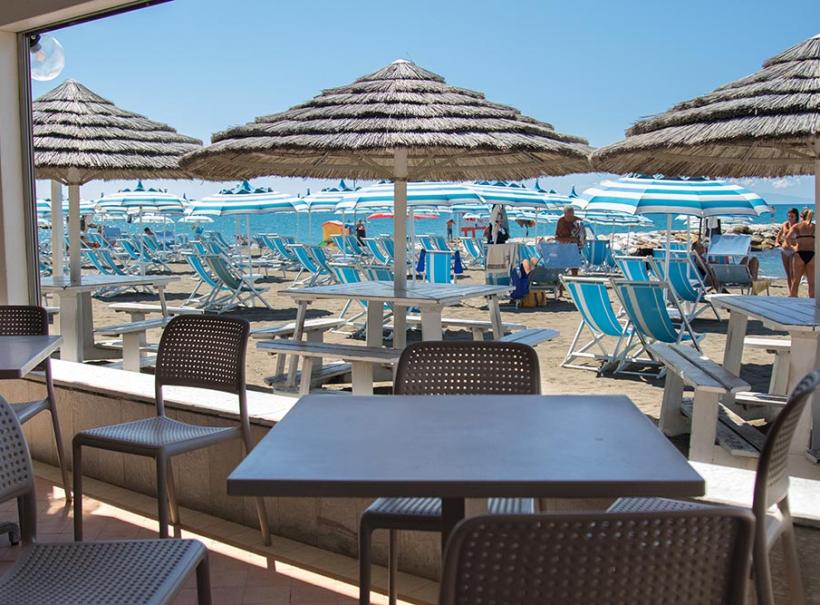 Spiaggia con ombrelloni e sedie a sdraio, vista da un bar all'aperto.