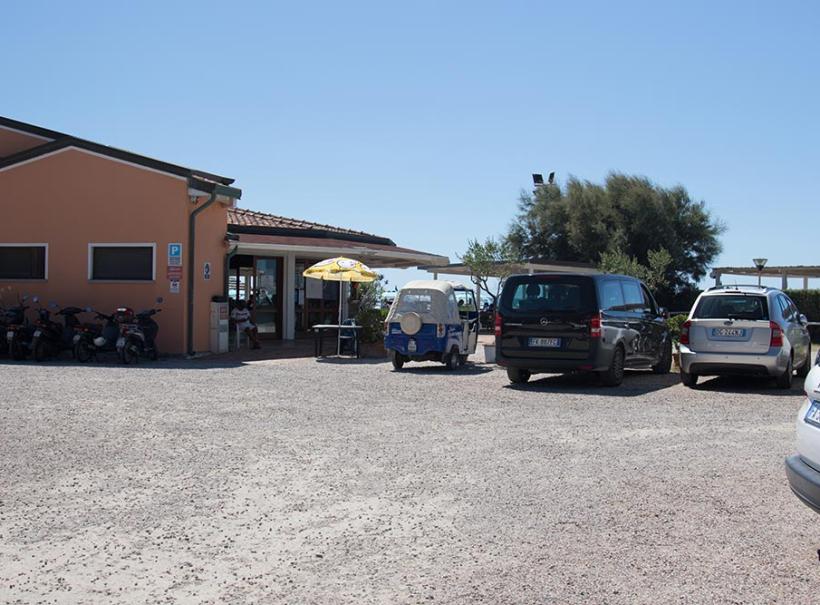 Parcheggio di fronte a un ristorante con auto e scooter, giornata soleggiata.