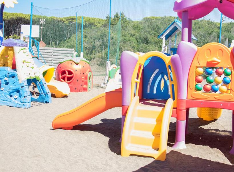 Parco giochi colorato con scivoli e strutture per bambini su sabbia.