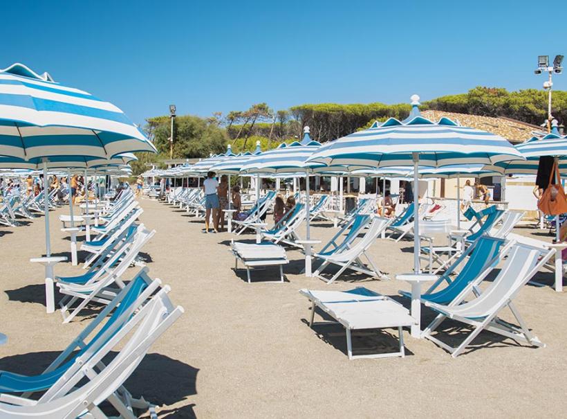 Spiaggia con ombrelloni e sdraio bianche e azzurre sotto il sole estivo.