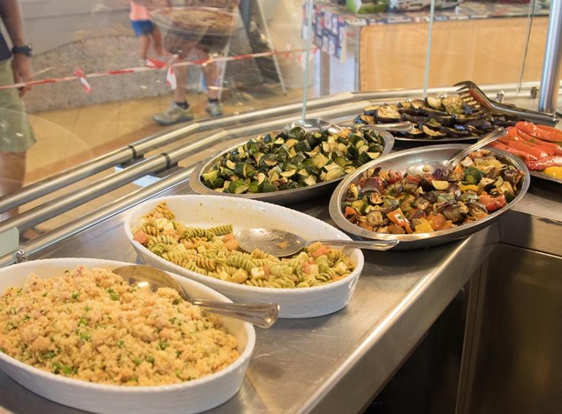 Buffet con insalate di pasta, couscous e verdure grigliate in piatti da portata.