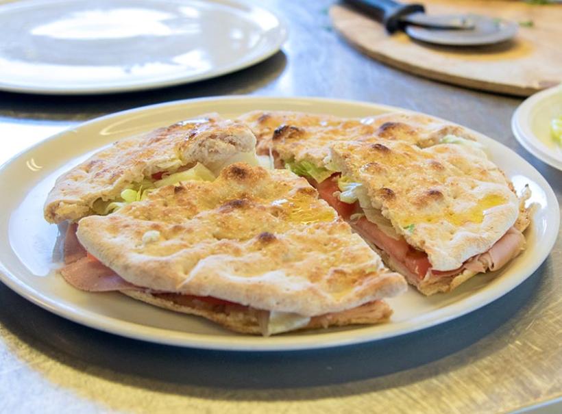 Focaccia farcita con prosciutto, lattuga e pomodoro su un piatto bianco.