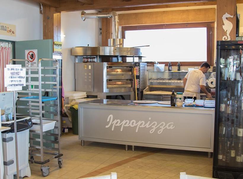 Interno di una pizzeria con forno, bancone e frigo per bevande.