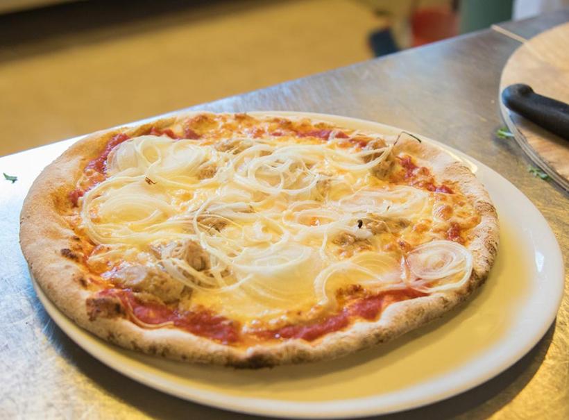 Pizza con cipolle e tonno su piatto bianco, su tavolo di metallo.