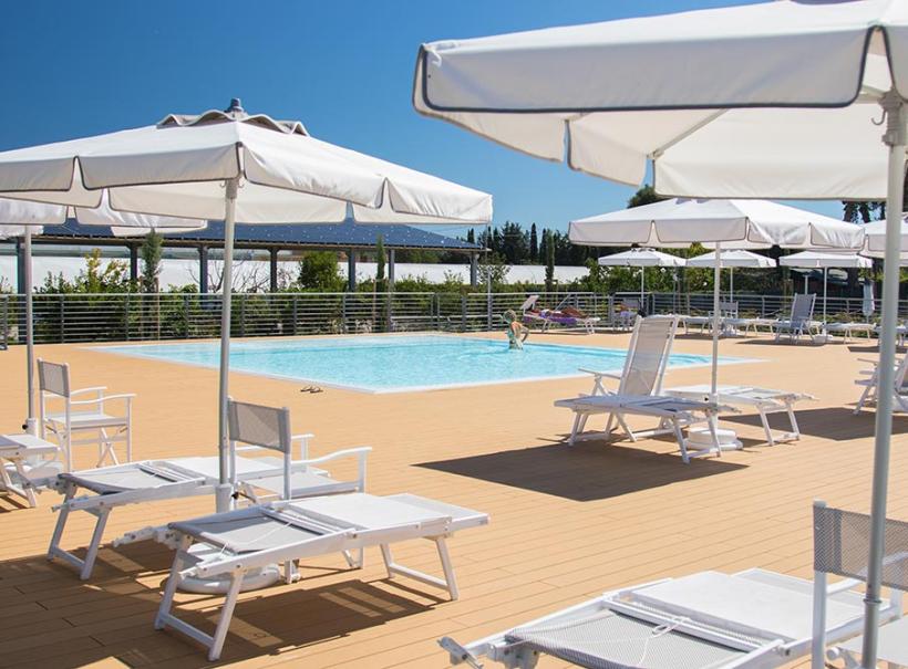 Piscina all'aperto con lettini e ombrelloni bianchi su terrazza in legno.