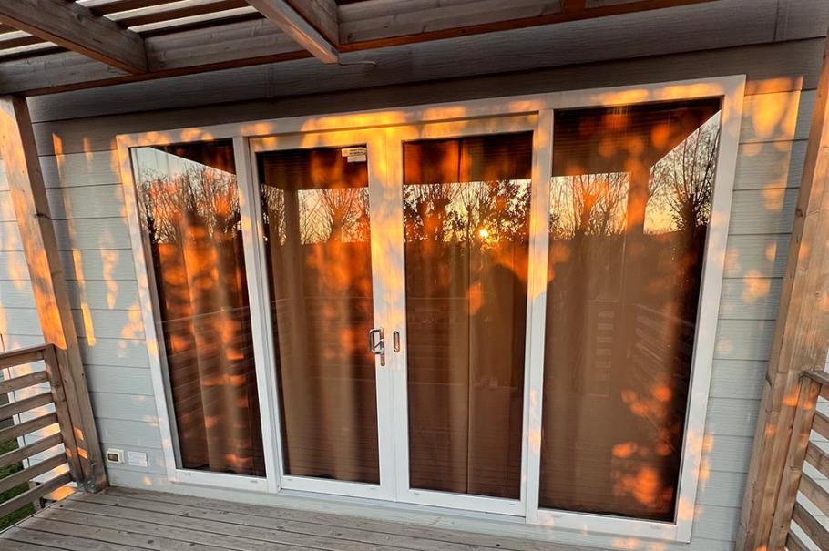 Terrazza in legno con porte finestre, illuminata dal tramonto.