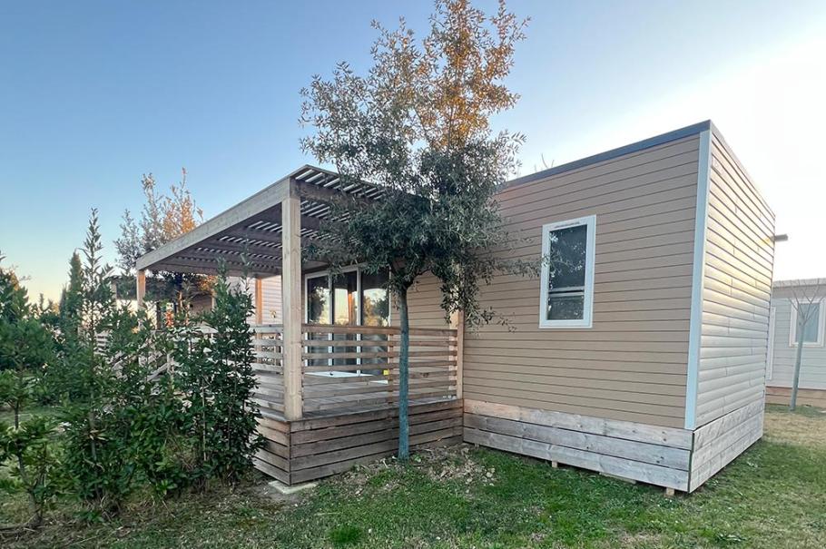 Casetta in legno con veranda, circondata da prato e alberi.