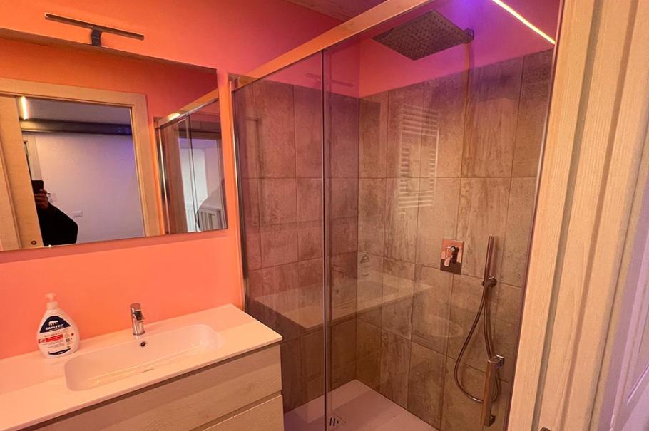 Bagno moderno con doccia in vetro, illuminazione a LED e lavabo sospeso.