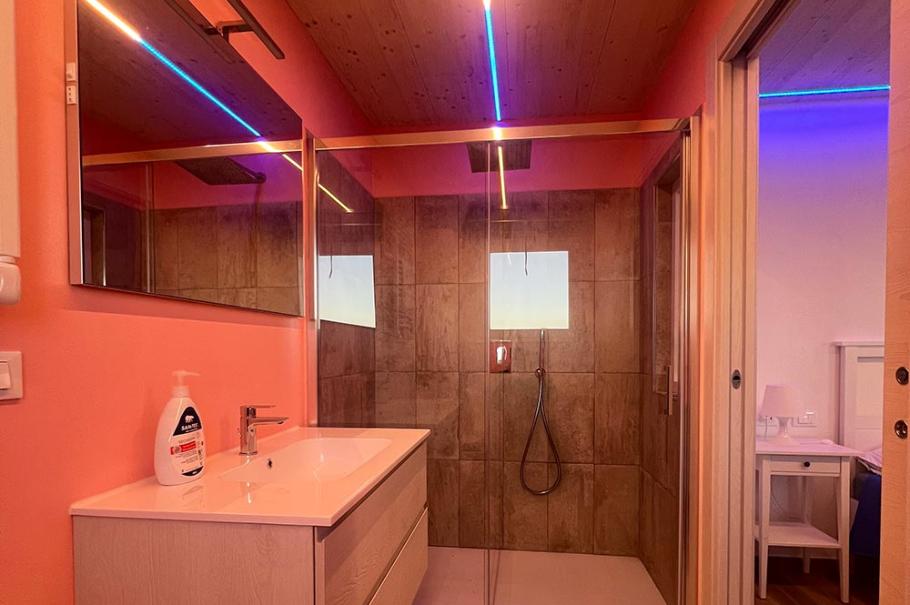 Bagno moderno con doccia a vetro, illuminazione LED e pareti color pesca.