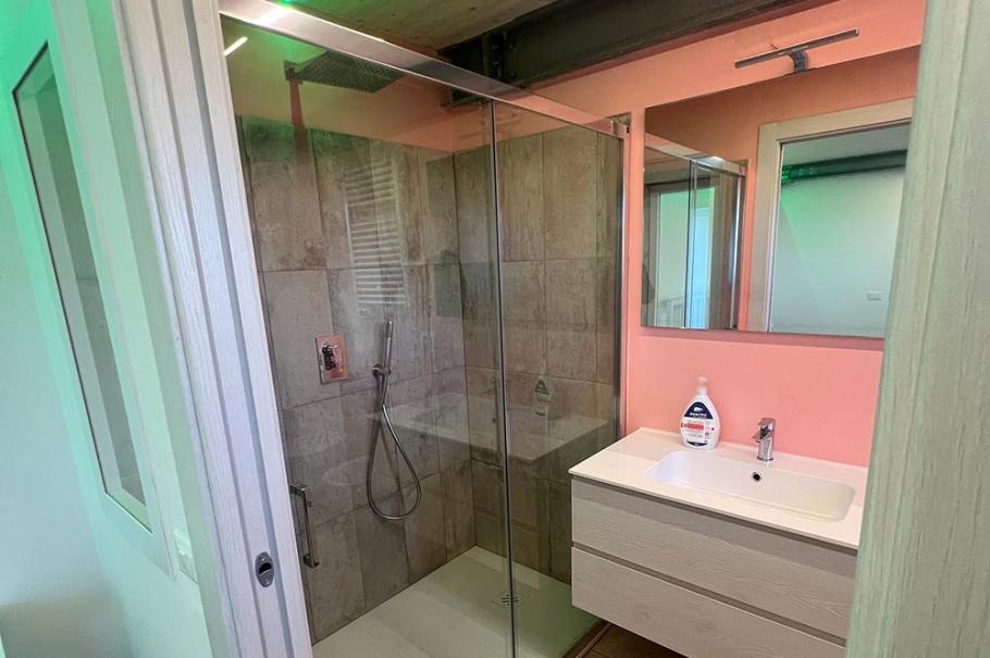 Bagno moderno con doccia in vetro, lavandino sospeso e illuminazione LED.